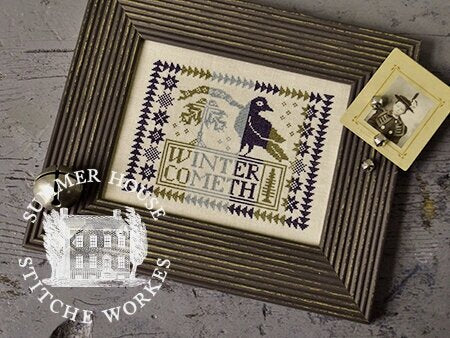 Framed cross-stitched piece with 'Winter Cometh' text and a bird design, on a textured surface with 'Summer Hill Stitch & Workes' branding.