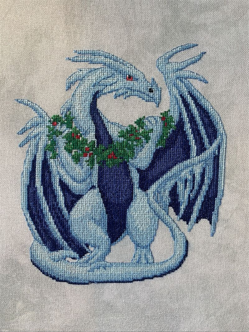 Embroidered design of a dragon holding holly leaves on fabric