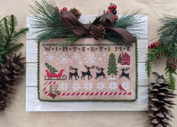 Christmas-themed cross-stitch design with reindeer, trees, and snowflakes on a wooden background.