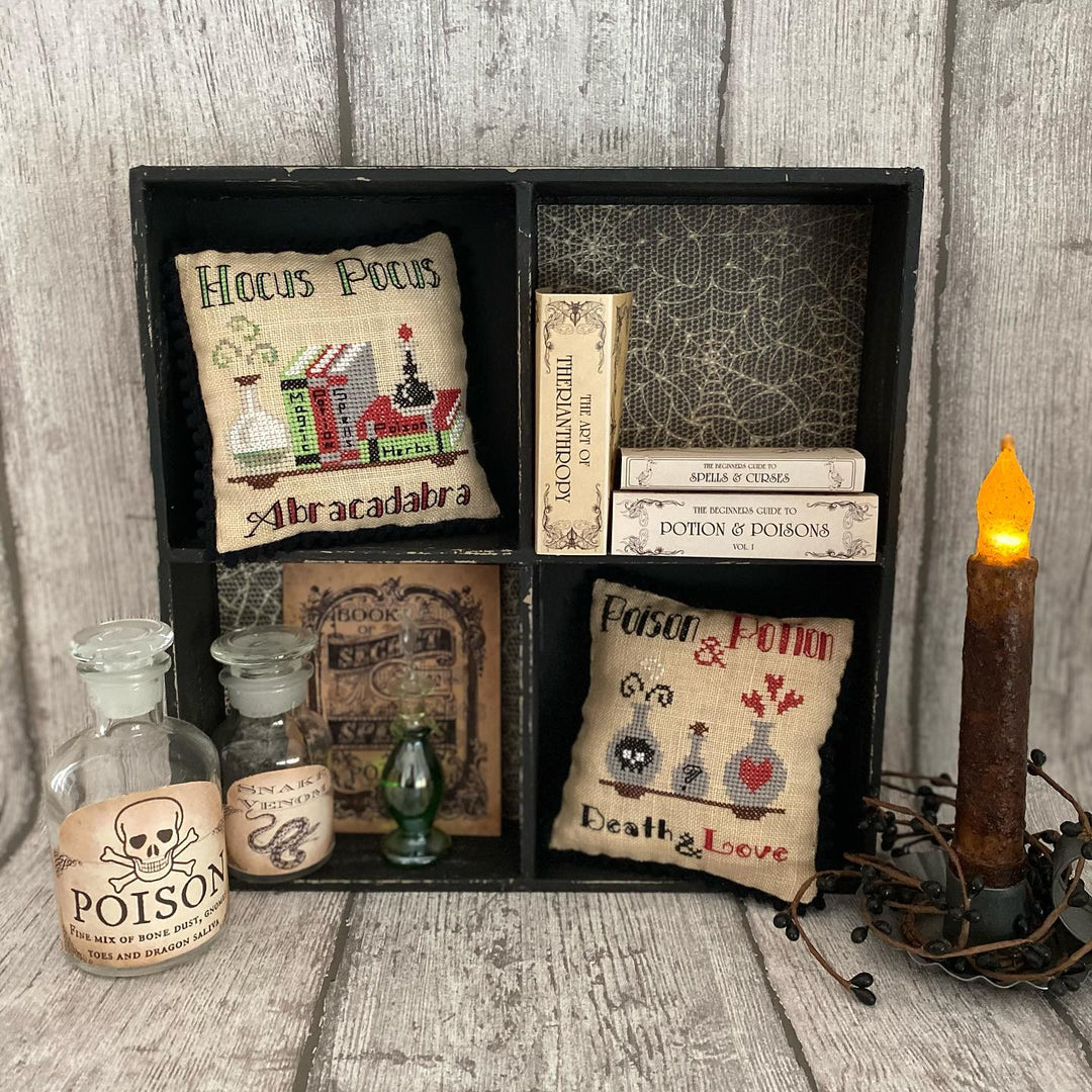 Decorative set with 'Hocus Pocus' and 'Abracadabra' pillows, poison bottles, and a candle on a wooden surface.