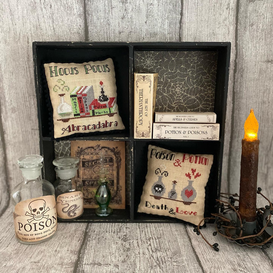 Decorative set with 'Hocus Pocus' and 'Abracadabra' pillows, poison bottles, and a candle on a wooden surface.