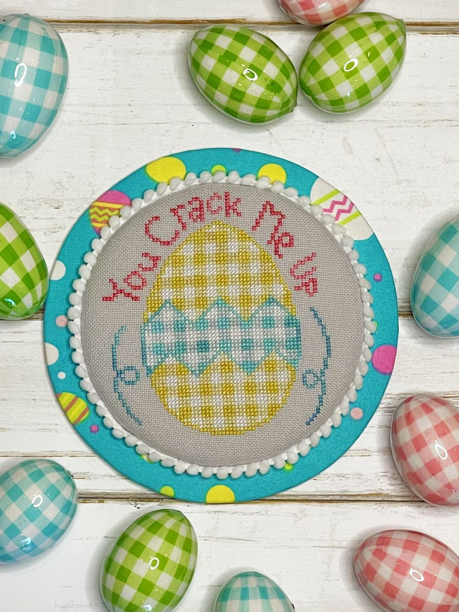Decorative Easter egg with cross-stitched design and checkered border on a wooden surface with colorful eggs.