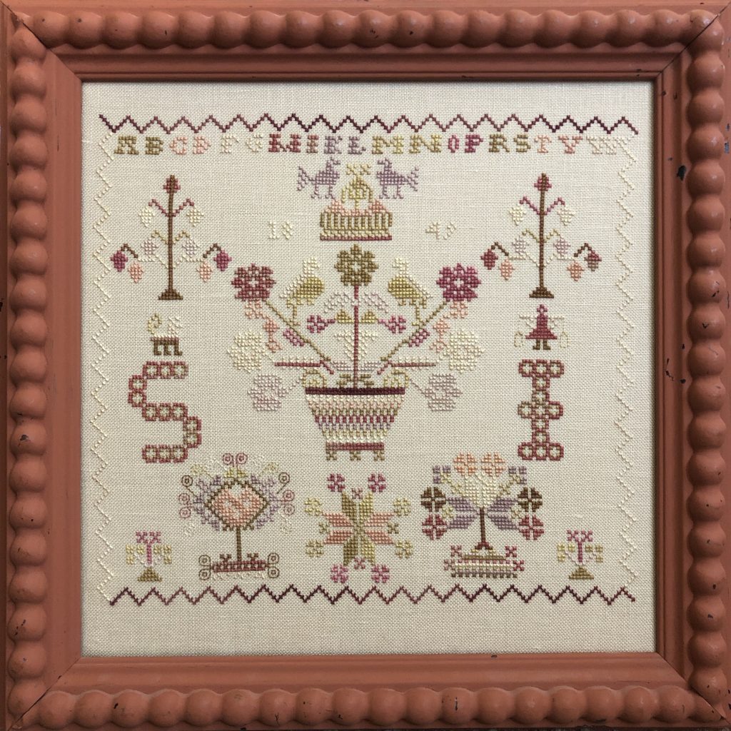Cross-stitched pattern with floral and geometric designs in a wooden frame.