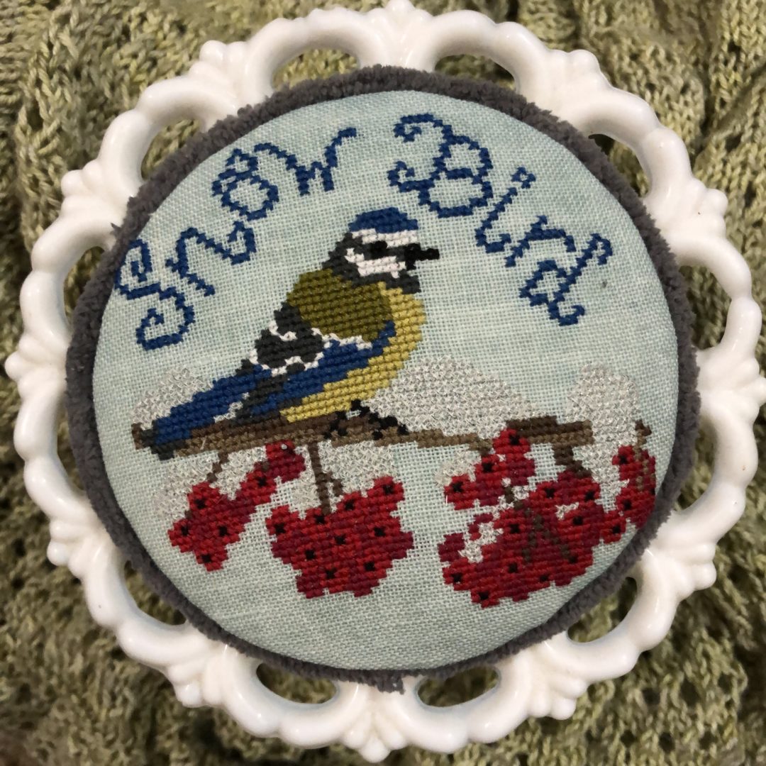 Embroidered patch with a bird and berries on a textured fabric background