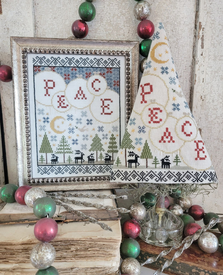Framed cross-stitched piece with 'PEACE' and Christmas-themed decorations.