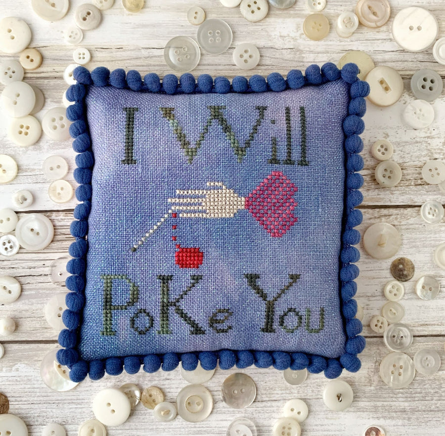 Cross-stitched pillow with 'I Will Poke You' text on a wooden surface with buttons.