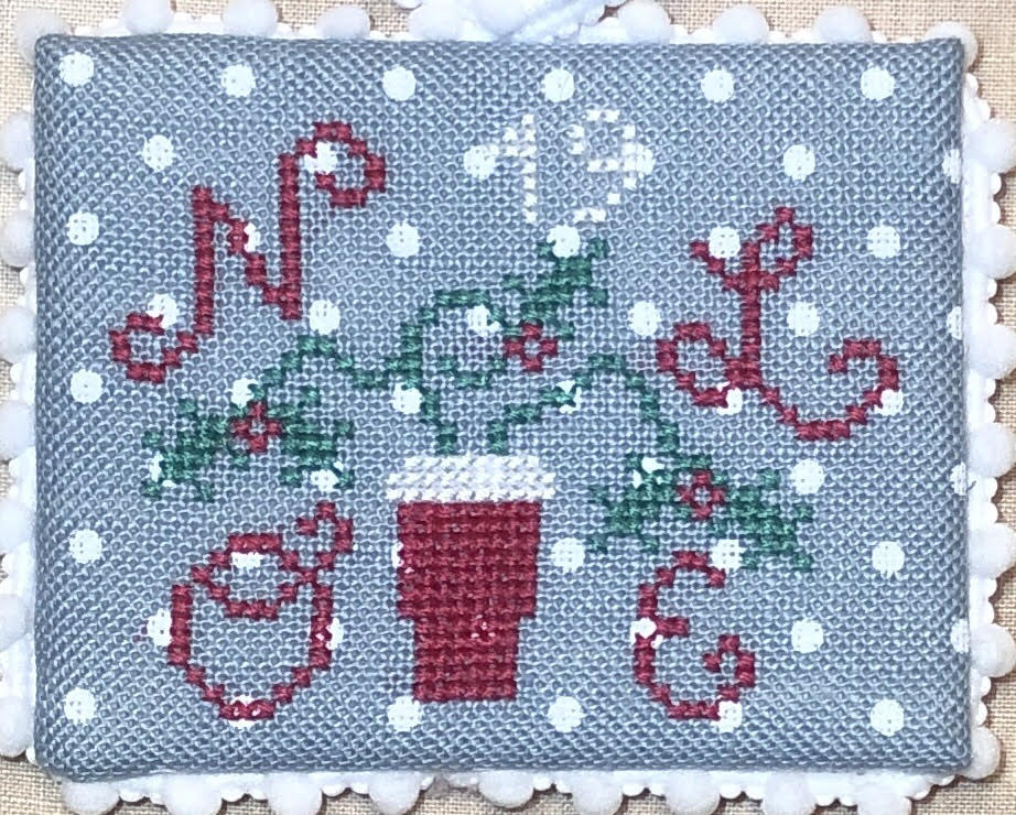 Cross-stitched design with a cup, candy canes, and snowflakes on gray fabric.