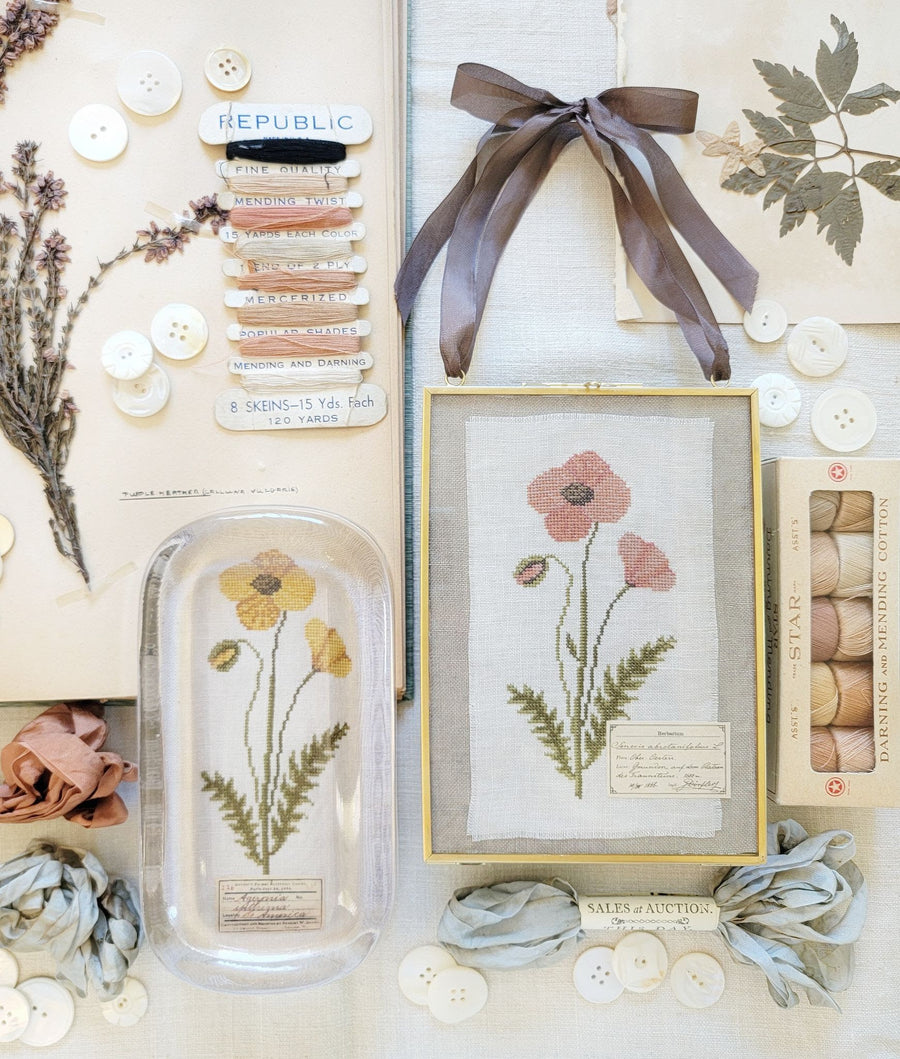 Collection of decorative items including framed artwork, pressed flowers, and ribbons on a neutral background.
