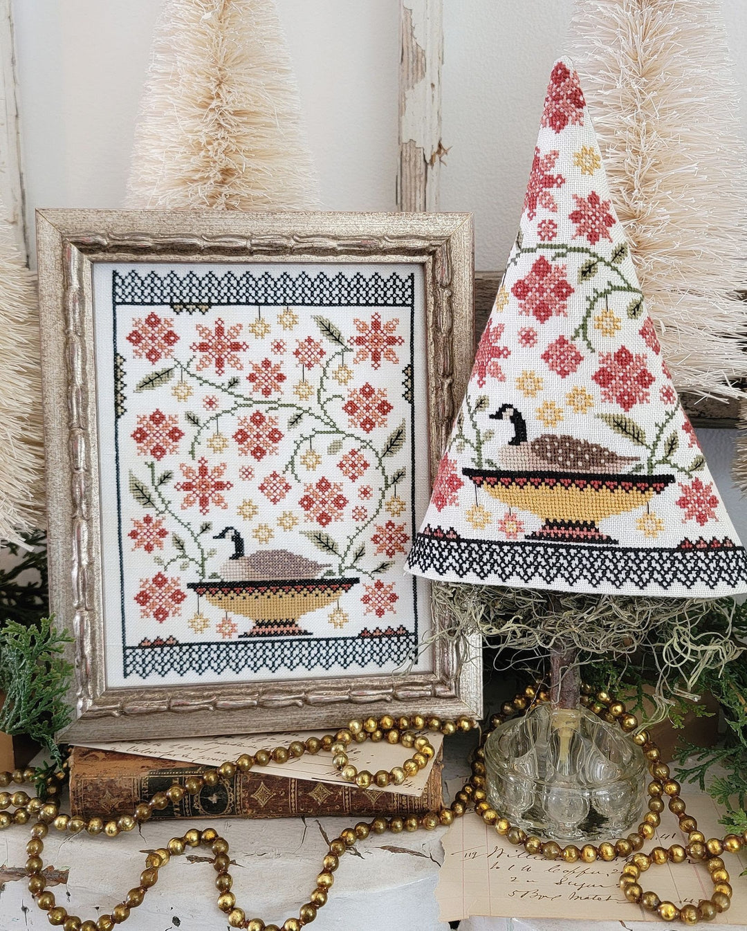 Decorative cross-stitched pieces with floral and nature-themed designs on a rustic wooden surface.