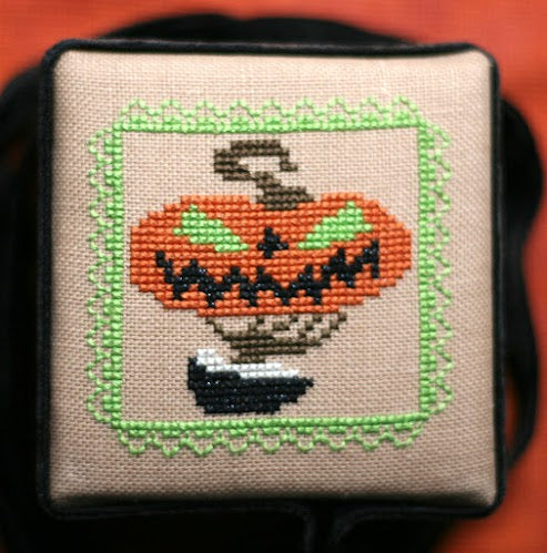 Cross-stitched pumpkin design on fabric with a black border