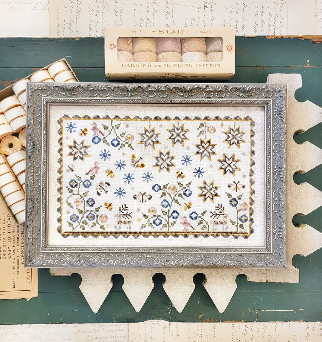 Framed cross-stitch pattern with decorative frame on a rustic wooden surface
